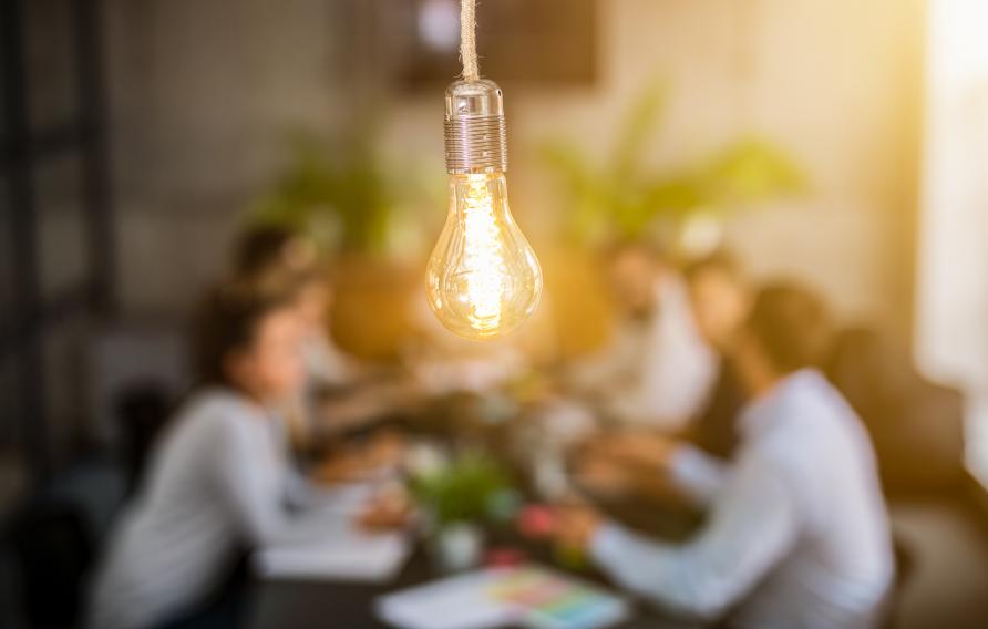 lightbulb in front of out of focus group of people at table