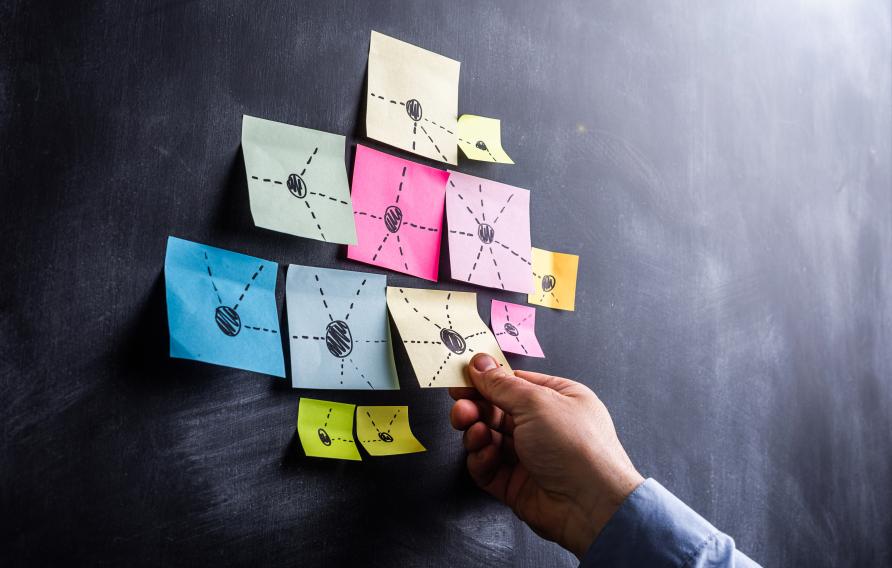 hand pulling sticky note off of blackboard with other sticky notes