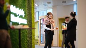 Jacobs women in an office talking in front of a green moss wall