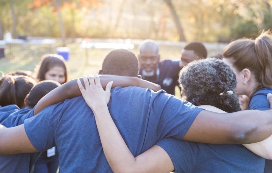 Group of diverse employees in a huddle with arms around each other