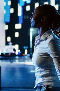 Smiling african american woman wandering around city boulevards during nighttime, pointing at interesting billboards on skyscrapers. Businesswoman strolling around streets illuminated by lamps