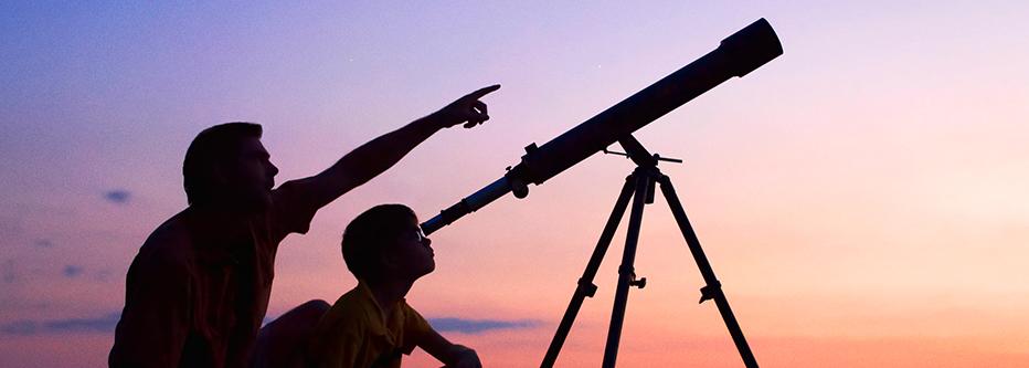 Man and son looking through telescope at dusk