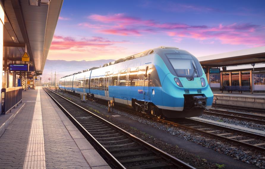 Stock image of a blue passenger train on tracks with pink and purple sunset