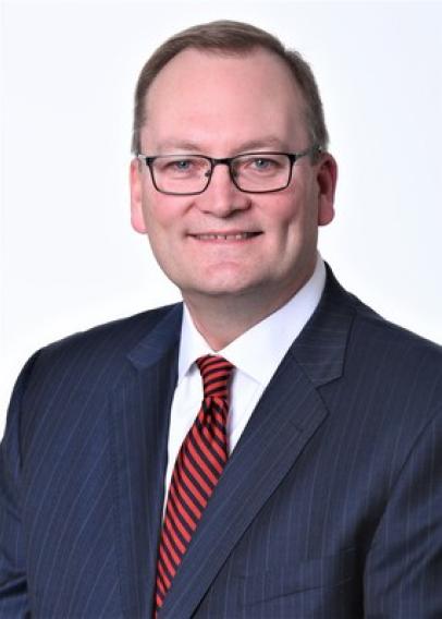 White man with glasses in a navy suit with red striped tie