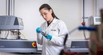 Dark haired woman in a white Jacobs lab coat working with lab equipment