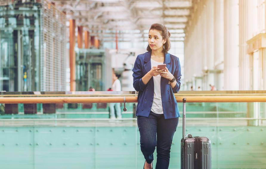 Stock image of business woman holding a cell phone in an airport with suitcase