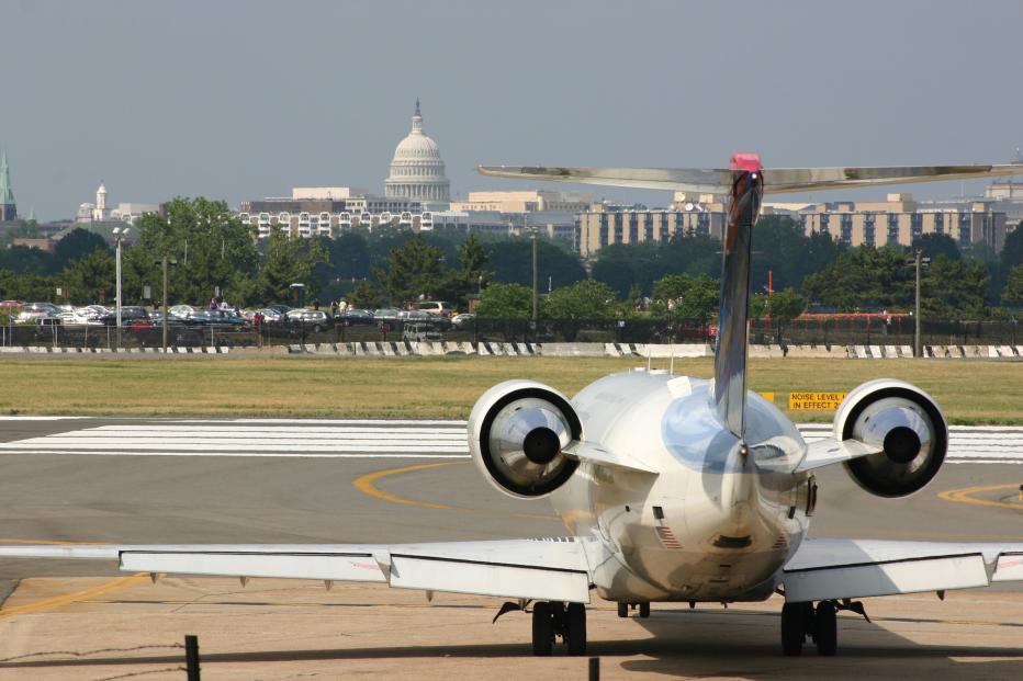 Airplane landing on a runway with Washington, DC skyline, including White House, in background