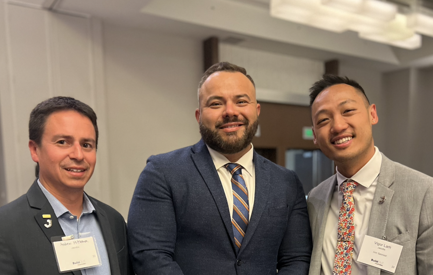 Three men in suits smile facing the camera